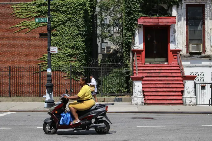 a woman on a moped rides through Harlem